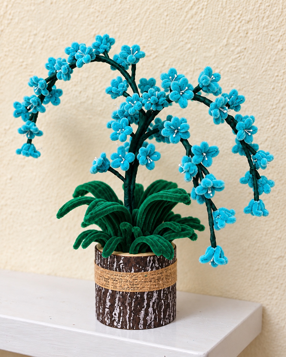 Handcrafted turquoise blue blossom arrangement with arching branches and green leaves in a rustic brown pot
