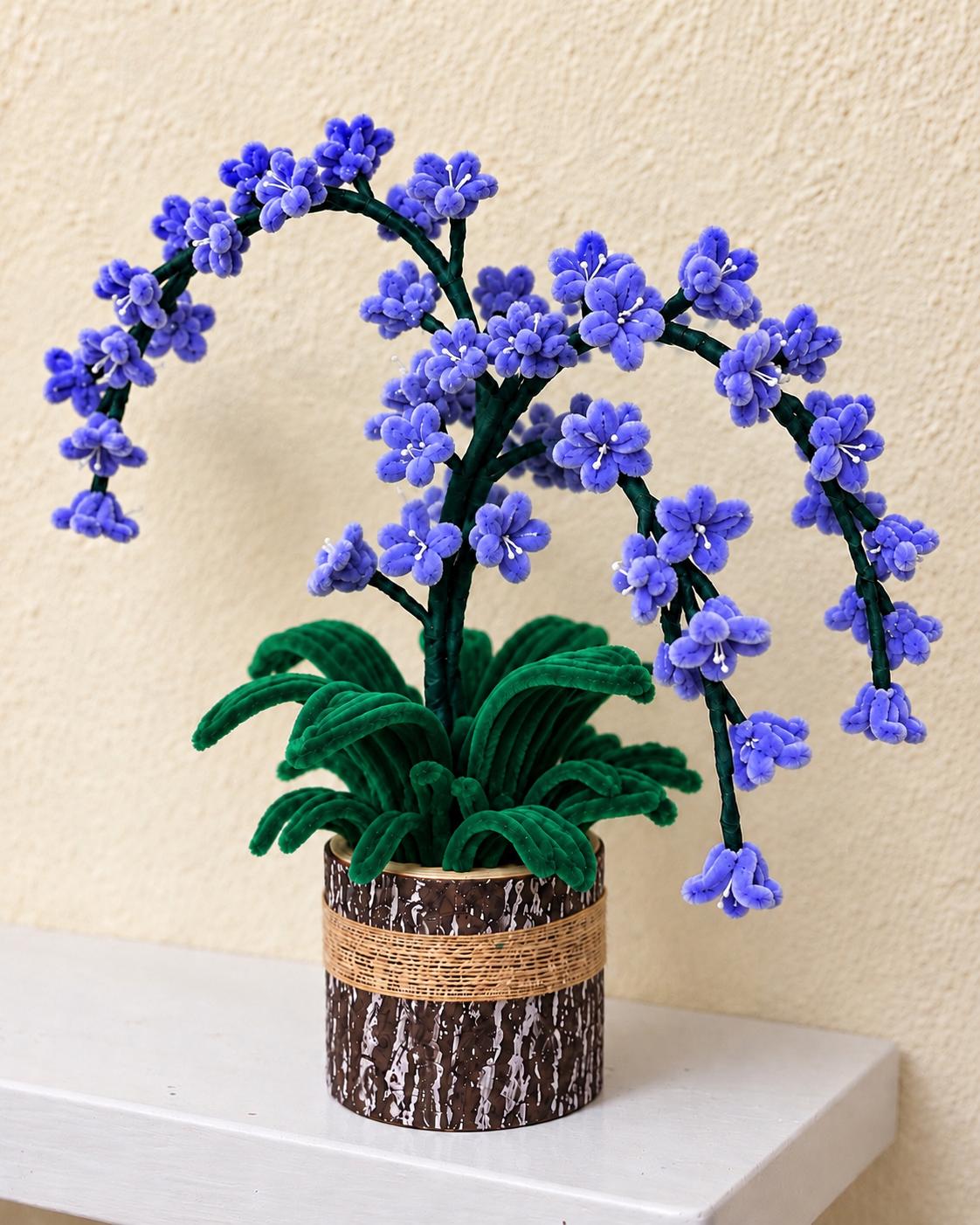 Blue-violet handcrafted blossom arrangement with arching branches and green leaves in a rustic brown pot