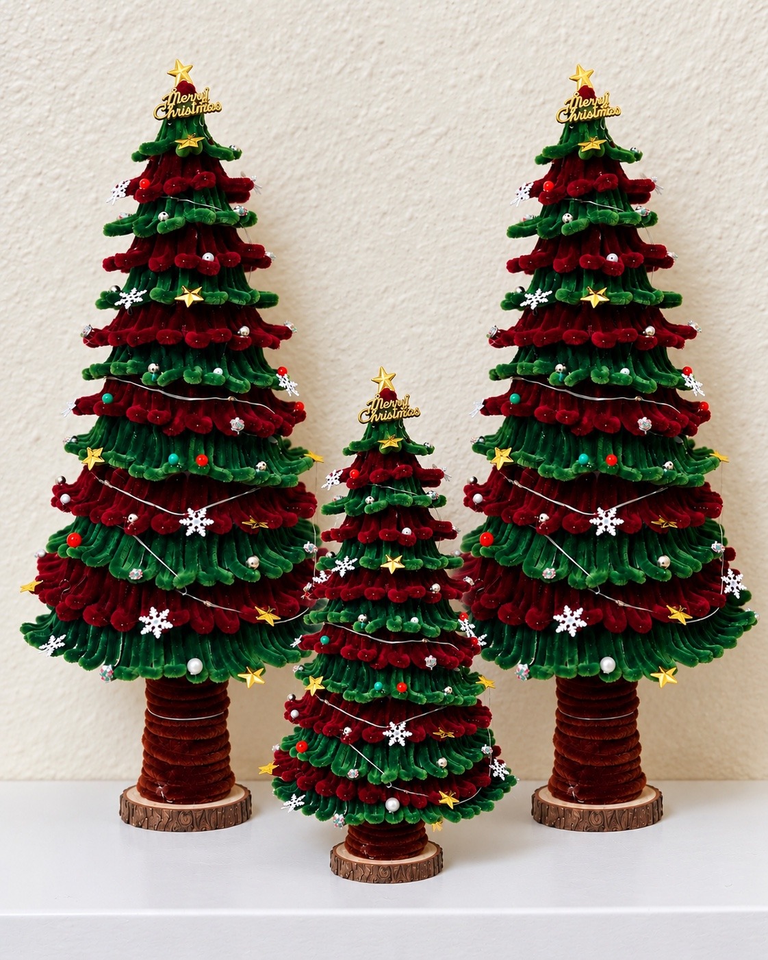 Two tall and one small handcrafted Christmas trees against a cream wall