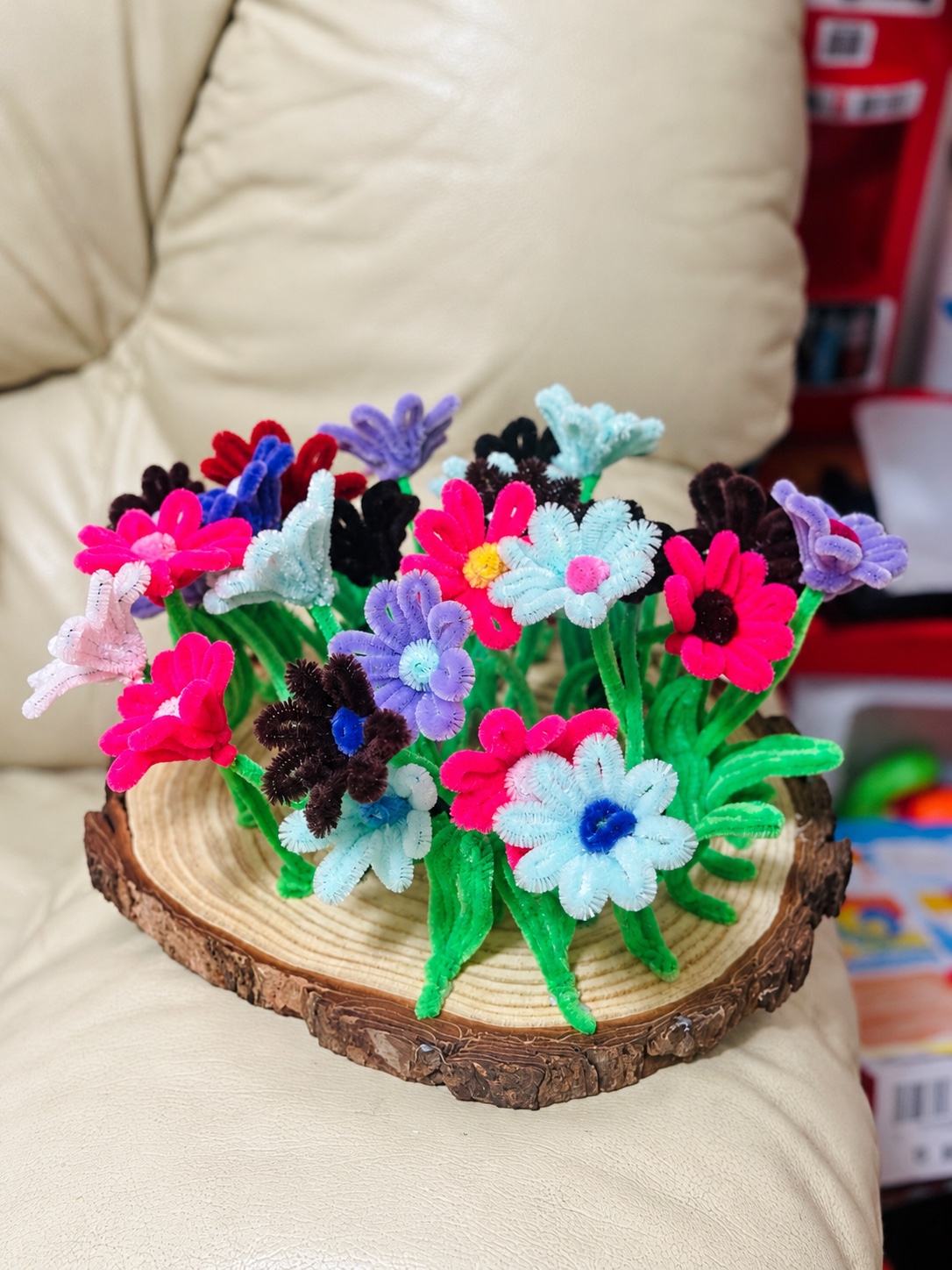 Colourful handmade chenille flowers arranged on a natural wooden base