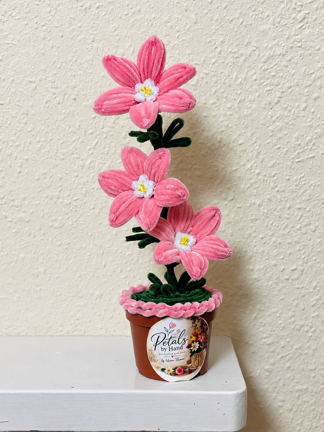 Three pink handmade flowers in a decorated pot